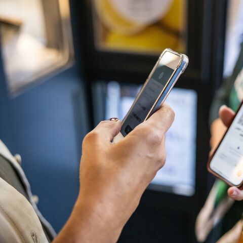 Two people hold smartphones; one scans a QR code on the other's screen in an everyday setting.