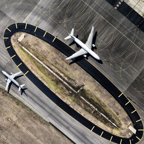 Two airplanes on an airport taxiway, one taxiing on a paved road, the other on a parallel runway.