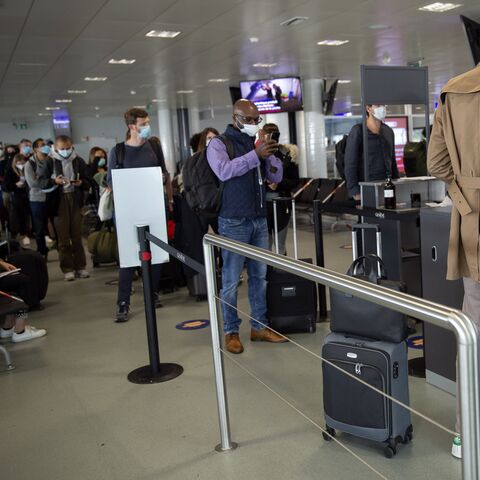 Des voyageurs portant des masques font la queue à l’aéroport devant un comptoir d’enregistrement où un homme est servi par une collaboratrice.
