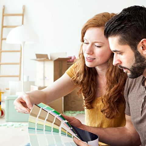Una coppia siede in una stanza ristrutturata e guarda insieme i campioni di colore per scegliere il nuovo colore delle pareti della propria casa.