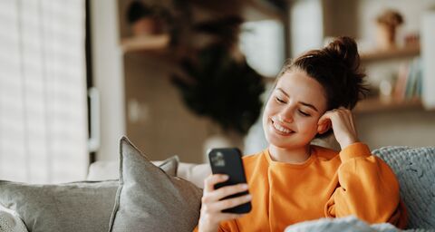 Junge Frau ruht auf Sofa mit Decke, scrollendes Smartphone.