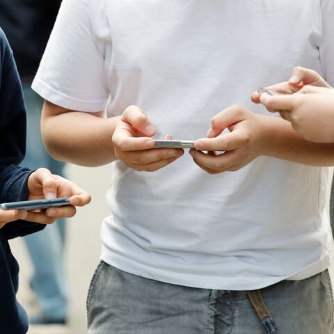 Trois jeunes hommes. Chacun se sert d’un téléphone portable avec ses deux mains.