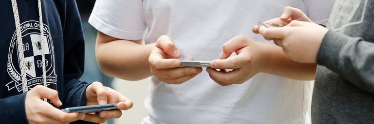 Drei junge Männer. Jeder bedient mit beiden Händen ein Mobiltelefon.