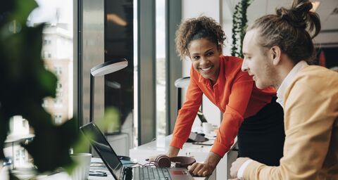 A young woman and a young man discuss a project in a bright workplace by the window.