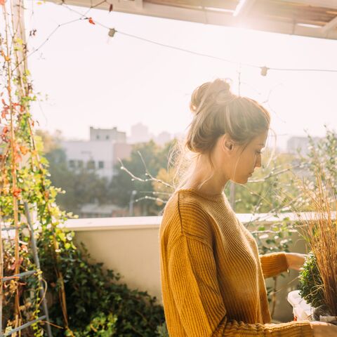 A woman is on her balcony in the sun, tending to her plants.