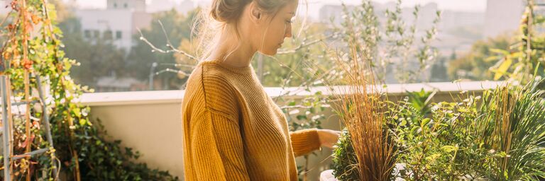 A woman is on her balcony in the sun, tending to her plants.