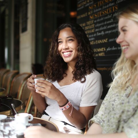 Zwei junge Frauen sitzen in einem Café und trinken gemeinsam ein Heissgetränk.