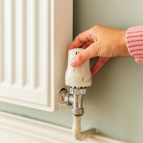 Dans la capture d’écran, on voit un radiateur sur un mur vert clair. Une femme en pull rose contrôle le thermostat.