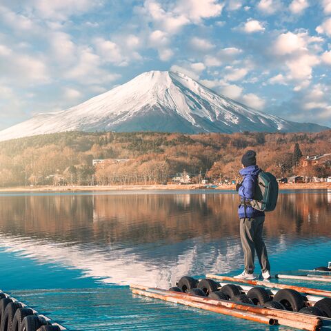 Ein Mann in Winterkleidung und Rucksack steht auf einem Steg und schaut den Berg Fuji an.