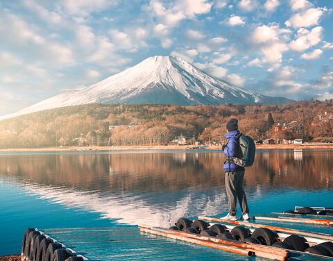 Ein Mann in Winterkleidung und Rucksack steht auf einem Steg und schaut den Berg Fuji an.