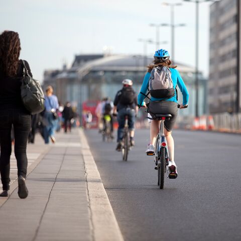 Un groupe de cyclistes, dont une personne portant un casque bleu et un sac à dos, roule sur une piste cyclable urbaine le long de hauts bâtiments.