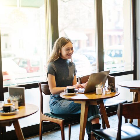 Une jeune femme joyeuse est assise dans un café et travaille sur son ordinateur portable.