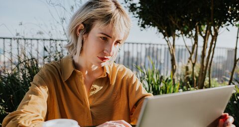 A young blonde woman is sitting on the balcony with her laptop.