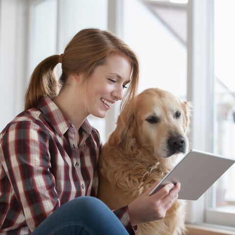 Laughing young woman sitting on the floor and looking at a tablet together with her dog