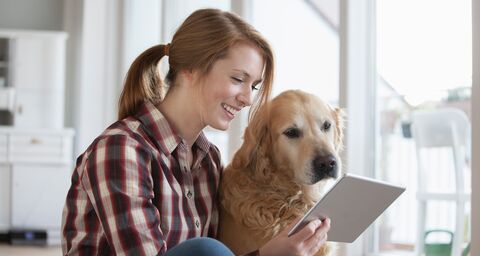Laughing young woman sitting on the floor and looking at a tablet together with her dog
