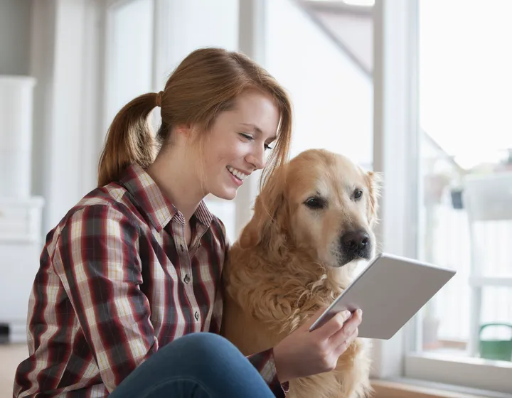 Laughing young woman sitting on the floor and looking at a tablet together with her dog