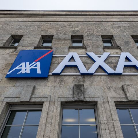 La photo montre le logo d’AXA Assurances sur un bâtiment gris avec plusieurs fenêtres à l’étage supérieur.