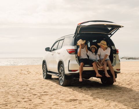 Eine Familie sitzt im offenen Kofferraum von einem Auto am Strand.