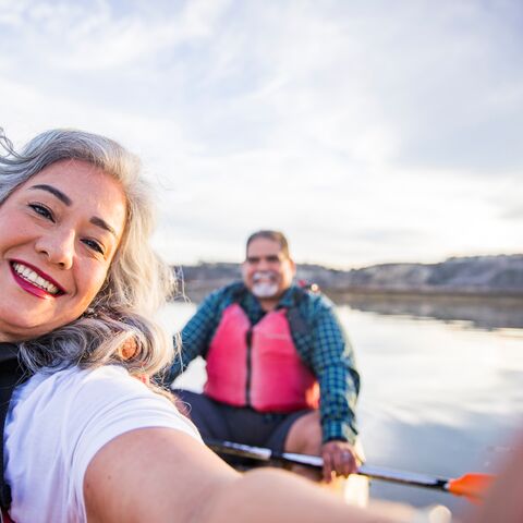 Una coppia è seduta in canoa. Lei scatta una foto di se stessa e del suo partner. Entrambi indossano giubbotti di salvataggio rossi.