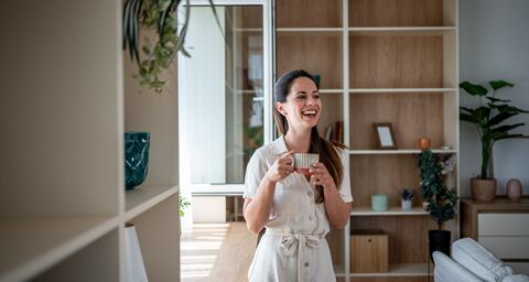 Junge Frau steht glücklich in ihrer modern eingerichteten Wohnung mit einer tasse in der Hand