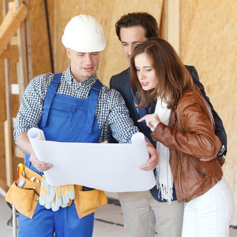 Un operaio edile mostra la pianta di una casa incompiuta a un uomo e a una donna e discute dei progressi della costruzione.