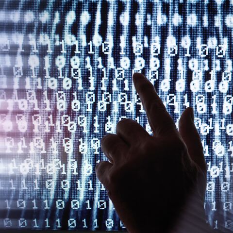 Eine Hand zeigt auf einen Bildschirm mit dicht gepackten, leuchtenden Binärzahlen, die in vertikalen Reihen angeordnet sind.