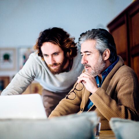 Due uomini lavorano insieme a un computer portatile, uno tiene un paio di occhiali mentre l'altro si guarda alle spalle.