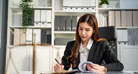 A young lawyer in a suit sits at a desk in an office and writes something in a file.