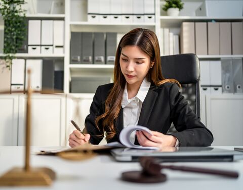 A young lawyer in a suit sits at her desk in an office and writes something in a file.