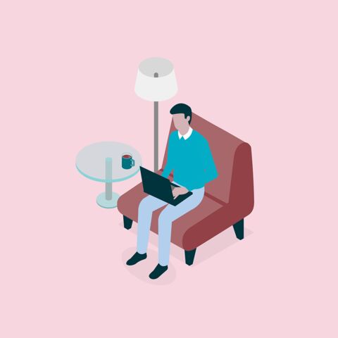 Une personne est assise sur un fauteuil rouge et travaille avec un ordinateur portable, à côté d’une table ronde avec une tasse, sous un lampadaire.
