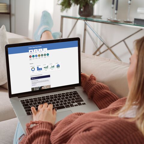 Una donna è seduta comodamente sul divano di casa con il suo laptop in grembo.