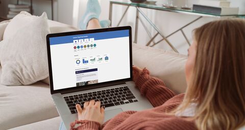 Una donna è seduta comodamente sul divano di casa con il suo laptop in grembo.