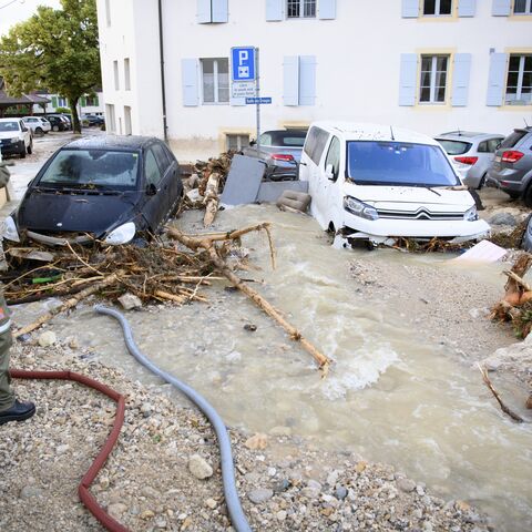 Un tratto di strada è allagato, le auto sono in acqua e i detriti sono sparsi. Un uomo in uniforme osserva la scena.