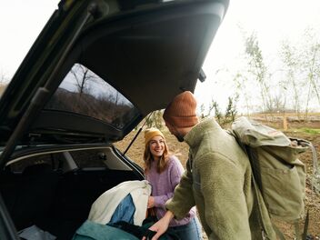 Woman and man pack their luggage out of the trunk and laugh at each other. 