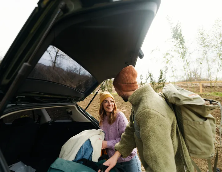 Woman and man pack their luggage out of the trunk and laugh at each other. 