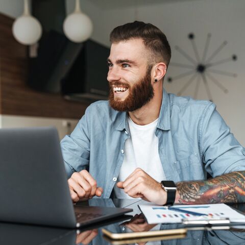 Un homme est assis à une table, sourit et travaille sur son ordinateur portable.