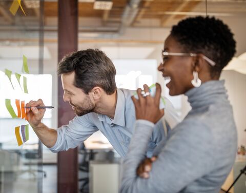 Two employees are happily standing in front of a flipchart.