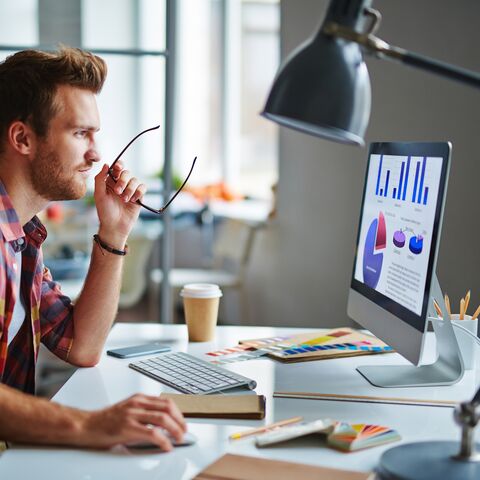 Ein junger Mann sitzt am Bürotisch und gestaltet etwas am Computer.