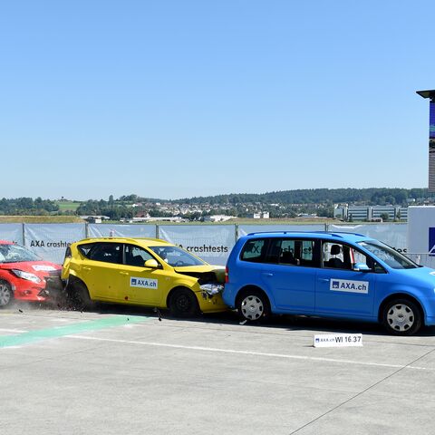 Drei Autos in den Farben Blau, Gelb und Rot prallen auf einem Testgelände während eines Crashtests der Firma AXA ineinander.