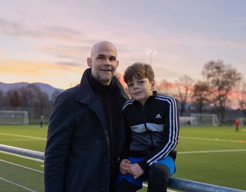 Ein Vater mit seinem Sohn. Sie sitzen am Rand eines Fussballfeldes.
