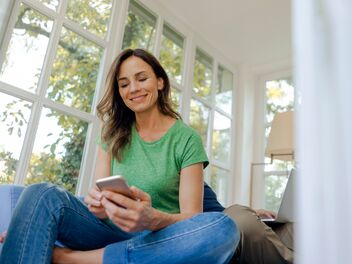 Una donna è sul divano e guarda tranquillamente il cellulare.