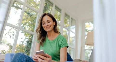A woman is sitting on the sofa, looking at her phone with a relaxed expression.