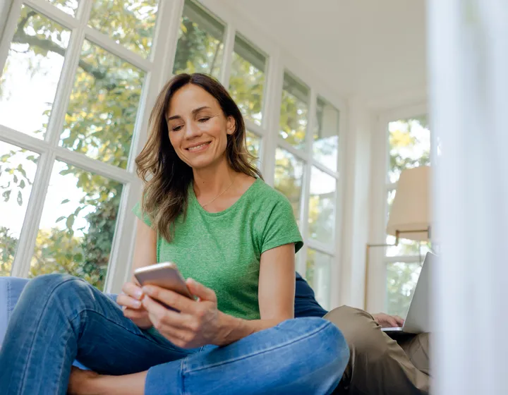 Una donna è sul divano e guarda tranquillamente il cellulare.