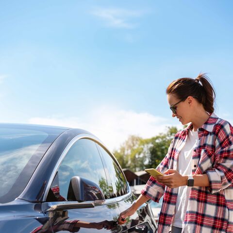 A young woman is opening her parked car.