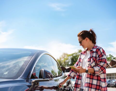 Eine junge Frau öffnet ihr parkiertes Auto.
