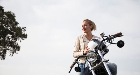 Une femme blonde est assise sur une moto et tient son casque dans ses mains.