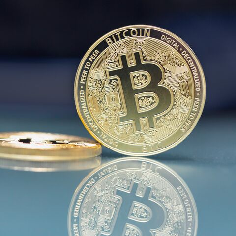 Eine glänzende Bitcoin-Münze steht aufrecht vor einer unscharfen zweiten Münze auf einem blauen Hintergrund.