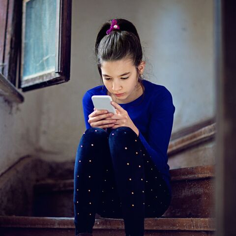 A girl sits on a wooden staircase and looks at her phone. 