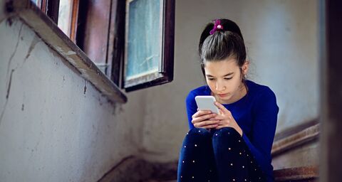 A girl sits on a wooden staircase and looks at her phone. 