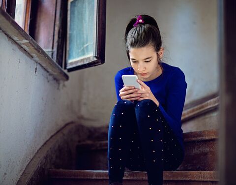 A girl sits on a wooden staircase and looks at her phone. 